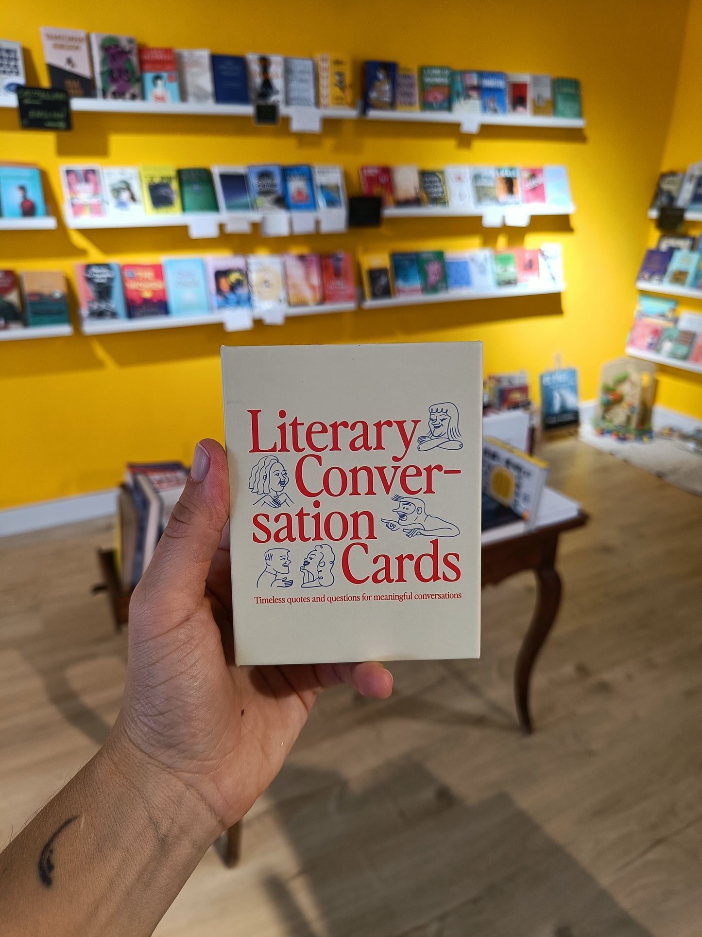 Hand holding 'Literary Conversation Cards' book in a bookstore setting