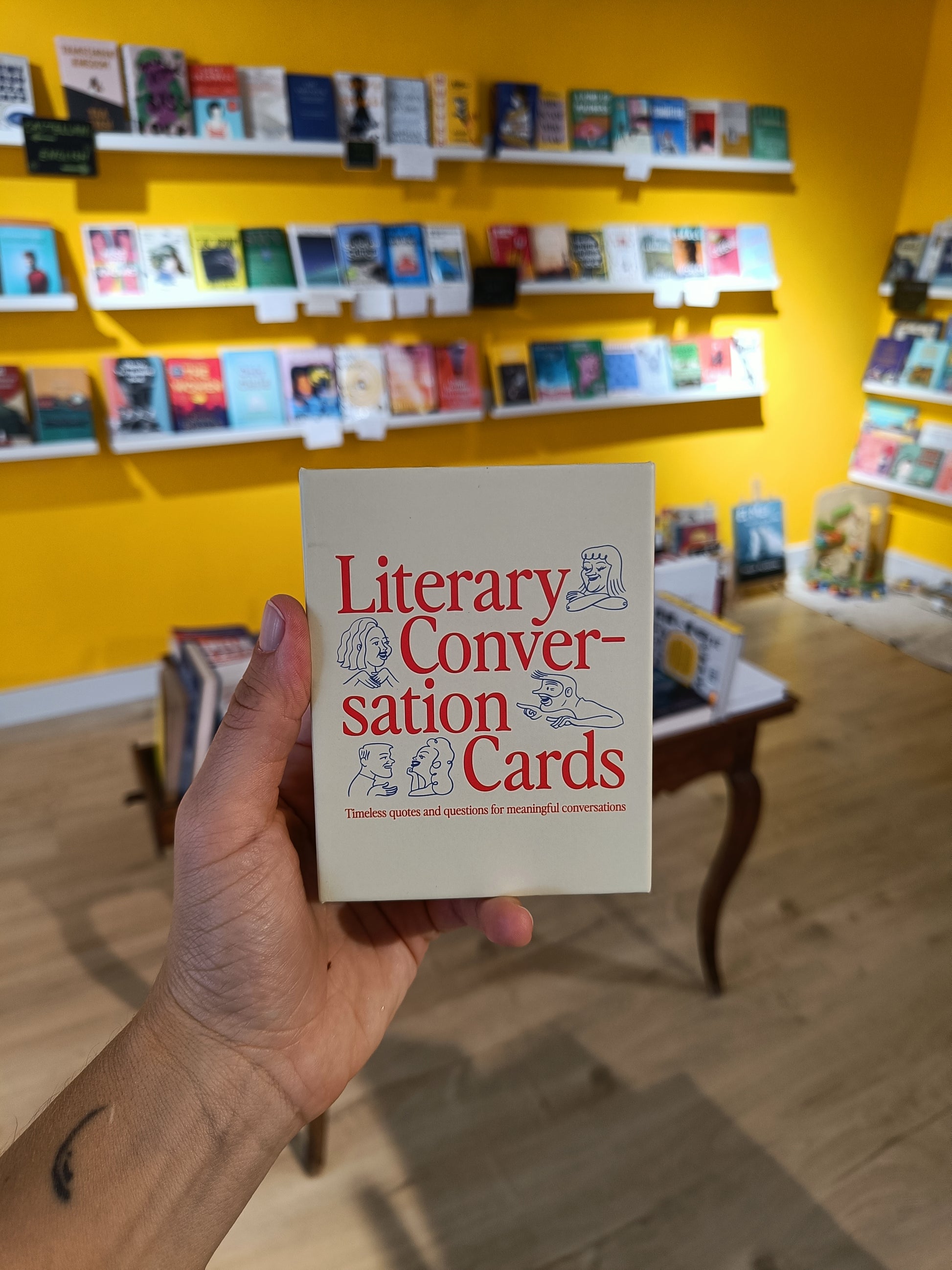Hand holding 'Literary Conversation Cards' book in a bookstore setting
