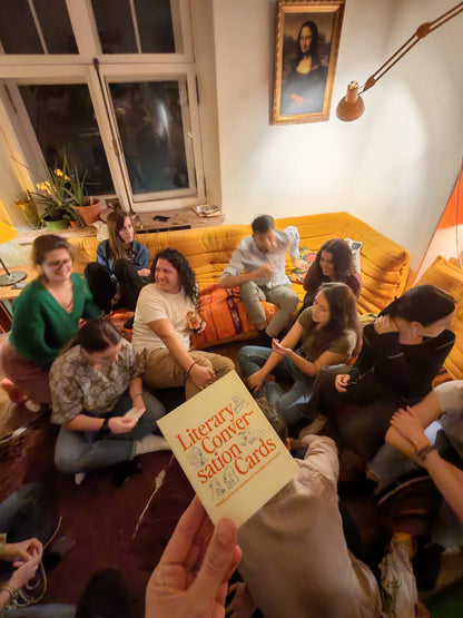 Group of friends in a cozy room with a person holding Literary Conversation Cards'